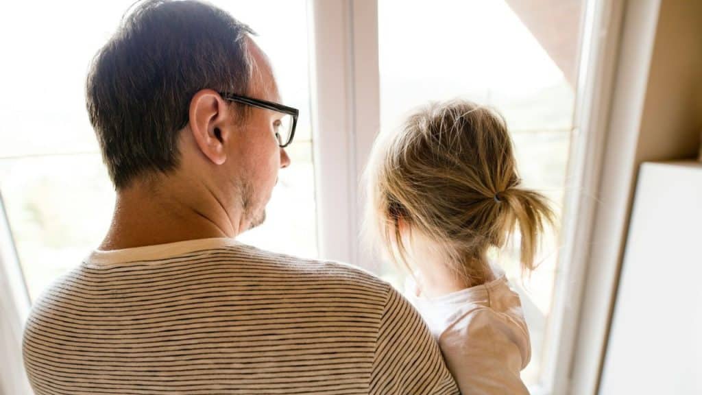 A man in a striped shirt and a child with blonde hair look out of a window.
