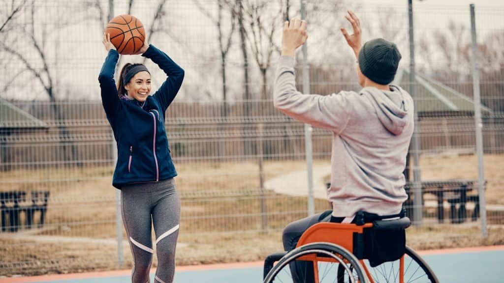Happy athletic woman having fun while playing basketball with a friend who uses a wheelchair.