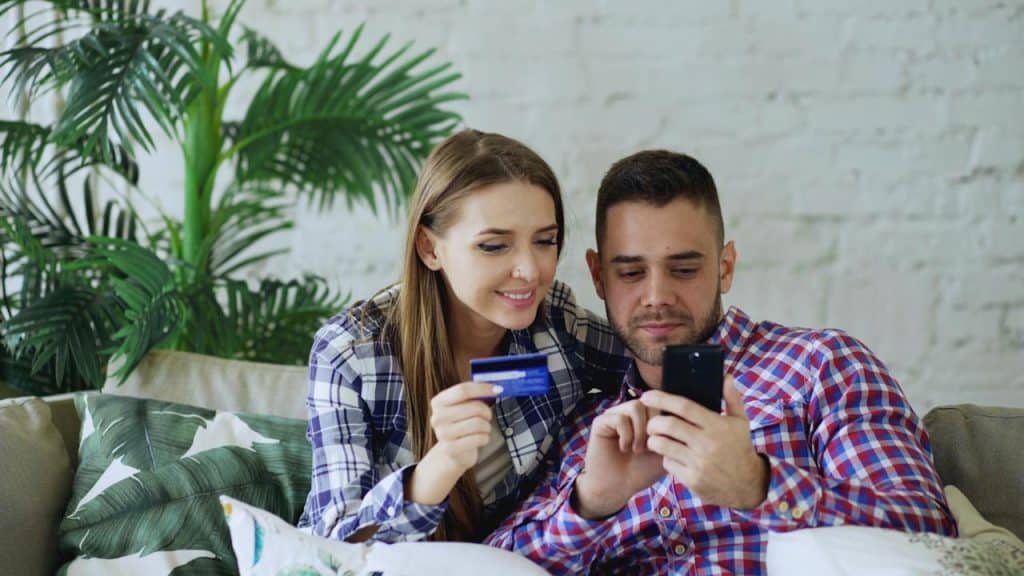 A man and woman using a phone and buying something with the woman’s credit card.