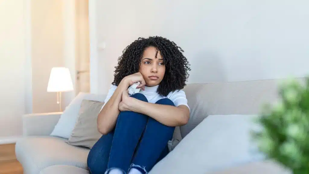 A woman sitting on the couch looking sad.