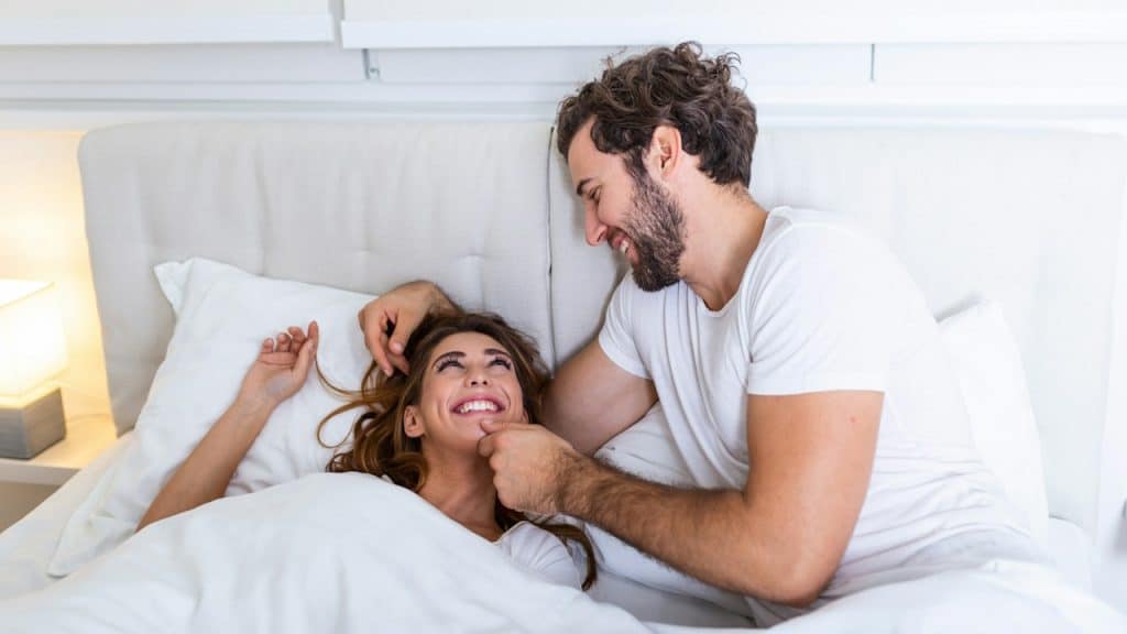 A man and woman smiling and having fun together while lying in bed.