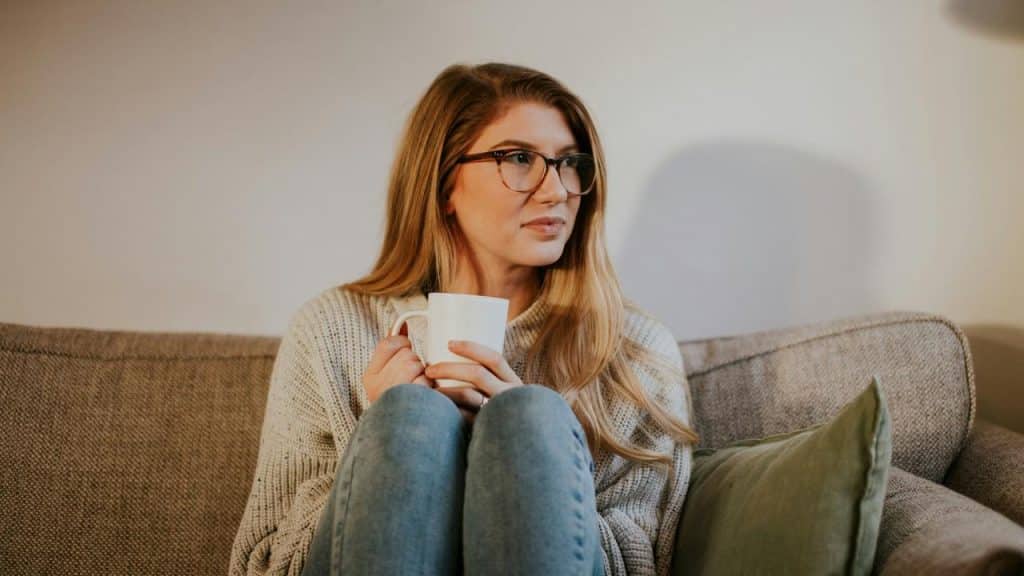 A woman sitting on a couch holding a mug and looking to the side.