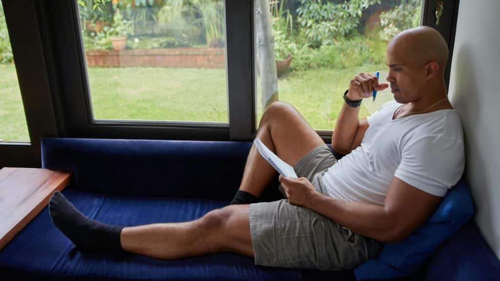 A man sitting on a blue couch looking out a window.