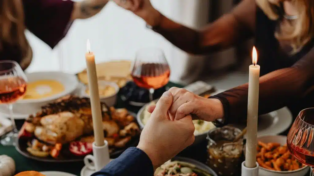 People holding hands in prayer over a candlelit dinner table.