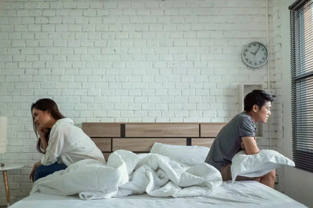 A couple sitting on the bed, ignoring each other.