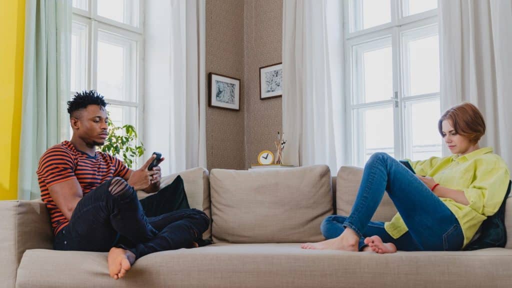A couple sitting on a sofa, but are both busy using their smartphones.