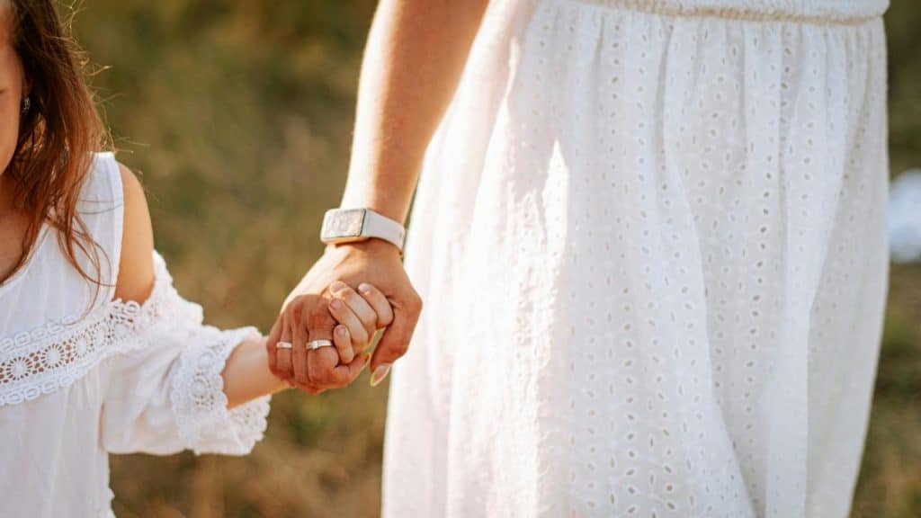 A woman in a white eyelet dress holding a child’s hand.