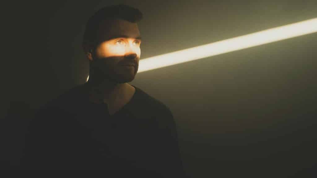 A man standing in shadow with a beam of light crossing his face.