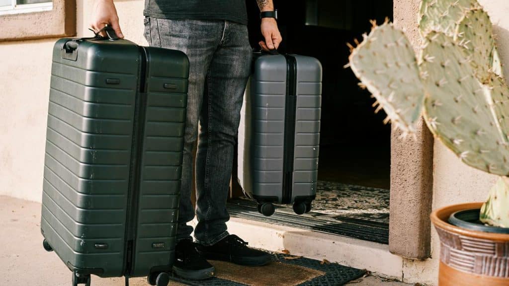 A person holding two suitcases while stepping out of a doorway.