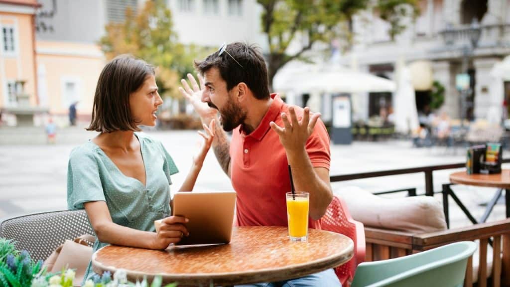 A man and woman have an expressive, intense conversation at an outdoor cafe table.