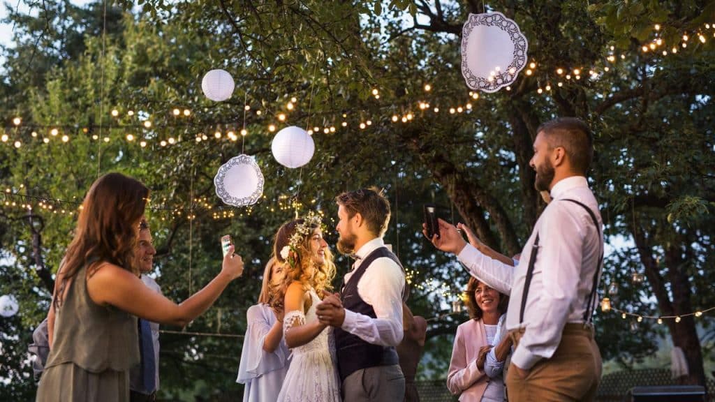 A couple dancing at an outdoor wedding under string lights as guests watch.