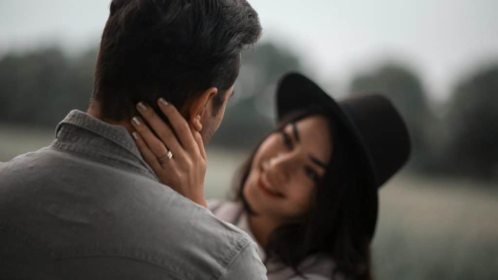A woman in a hat gently holding a man’s face outdoors.