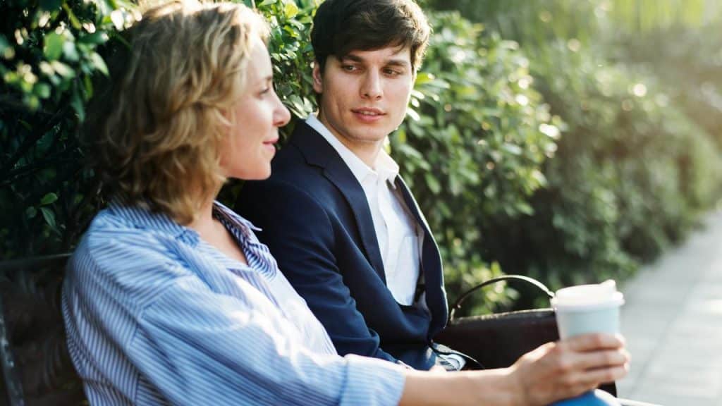 A couple talking on a bench with a coffee cup in hand.
