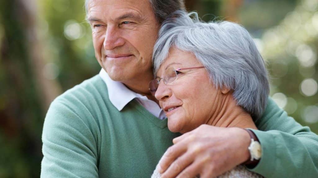 A close-up of an older couple embracing and looking peacefully into the distance.