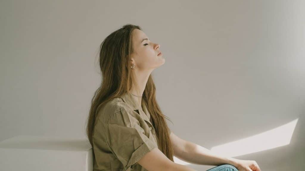 A woman sits with her eyes closed and her head tilted back against a wall.