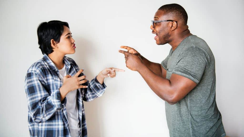 A man and woman stand facing each other, gesturing with their hands while talking.