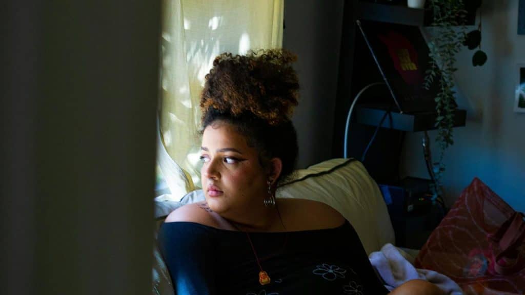 A person sitting by a window looking outside with a thoughtful expression.