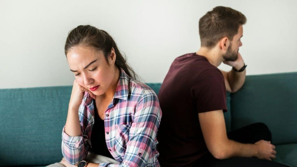 A man and woman sit back-to-back on a teal couch looking in opposite directions.