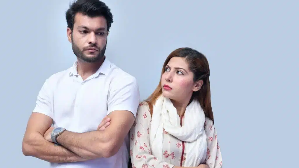 A man with crossed arms looks away while a woman looks back toward him.