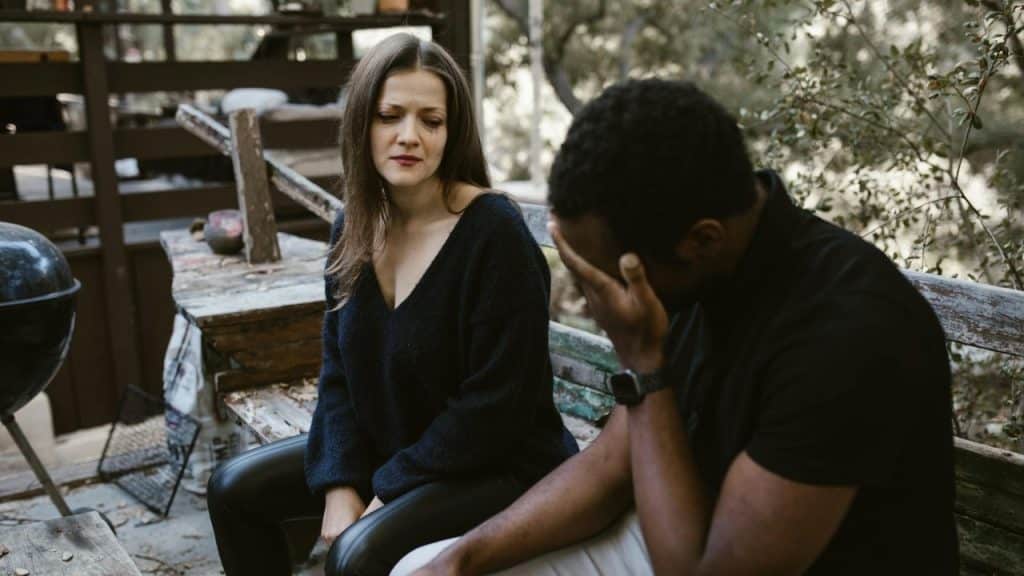 A woman in black looks at a man who is covering his face with his hand.