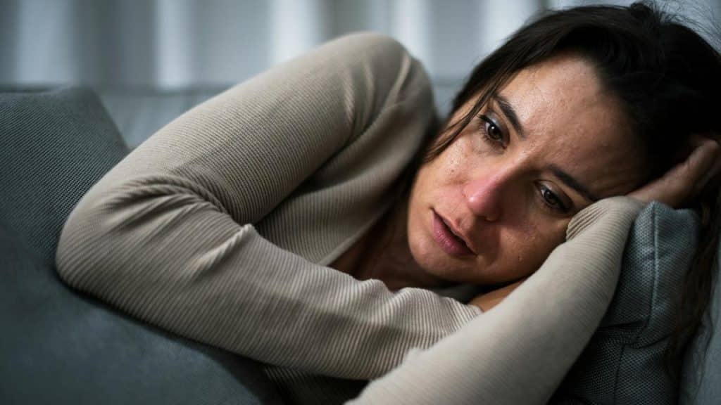 A woman lying on a couch with a tired, emotional expression.