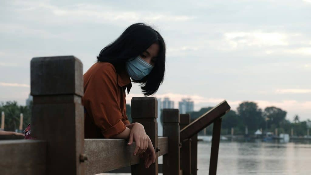 A woman in a red hoodie standing on a wooden dock during the daytime.