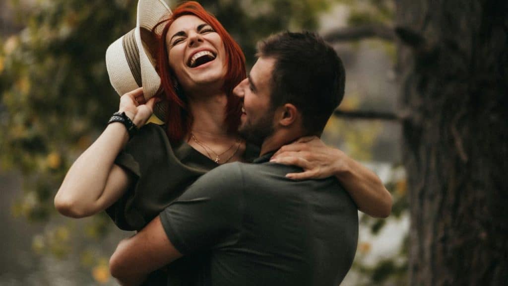 A joyful couple laughing together outdoors as they embrace.