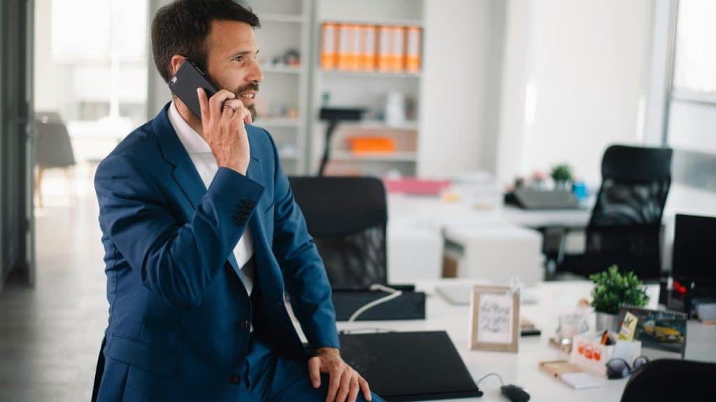 A man in a suit talking on a phone in a modern office.