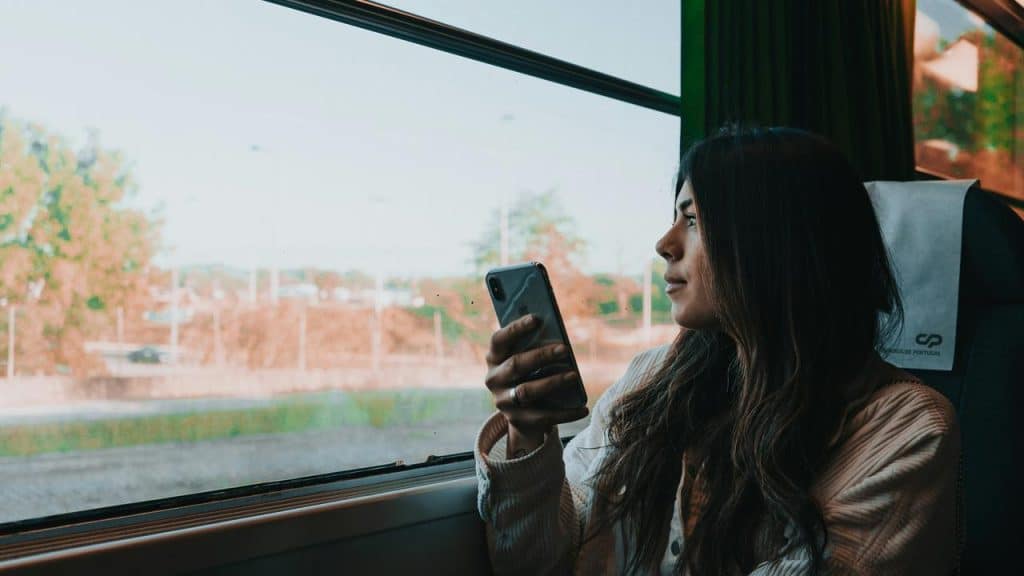 A woman holding a phone and gazing out a train window.