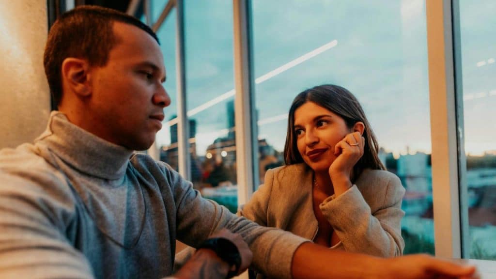 A woman rests her chin on her hand while looking at a man sitting beside her.