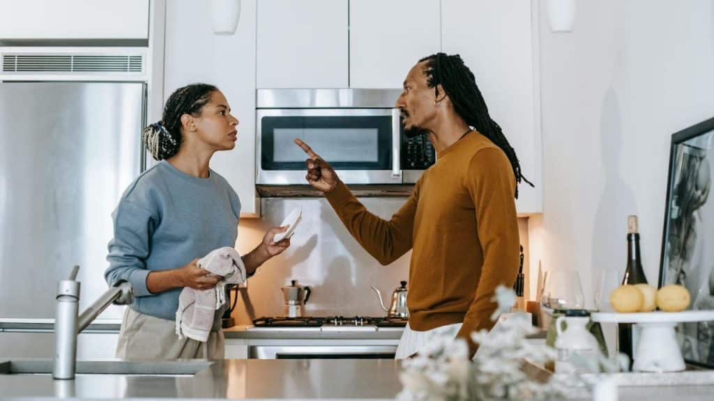 A man points a finger at a woman while standing in a kitchen together.
