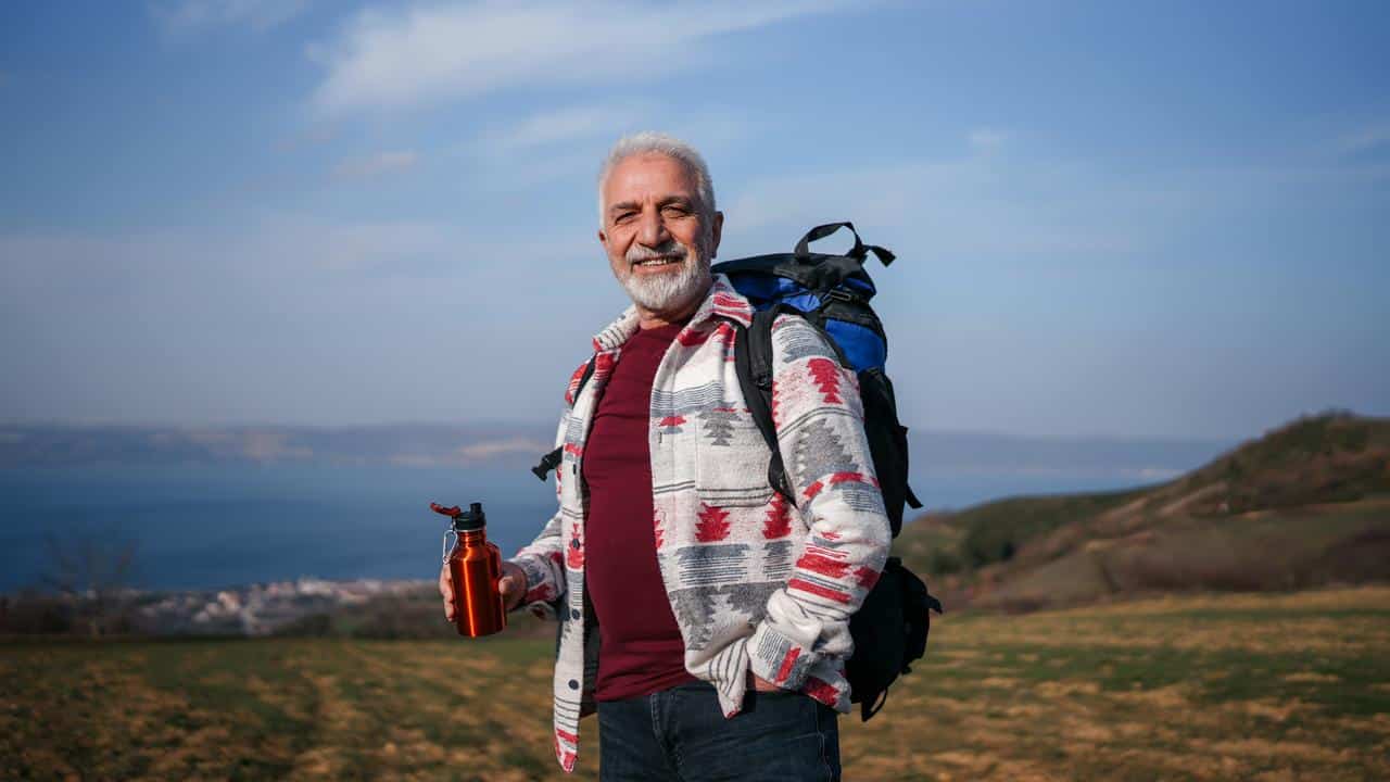 An older man hiking with a backpack and water bottle.