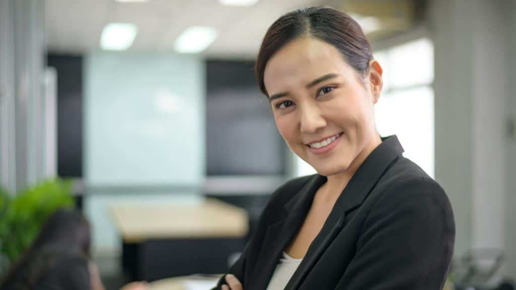 A woman in professional attire looking at the camera while standing in an office.