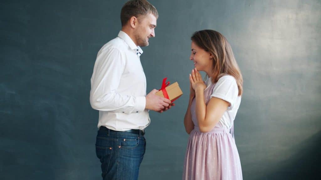 A man gives a woman a gift with surprised joy.