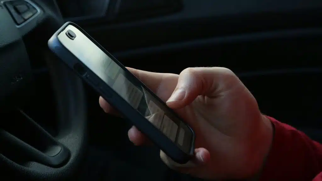 A hand holding a smartphone inside a car.