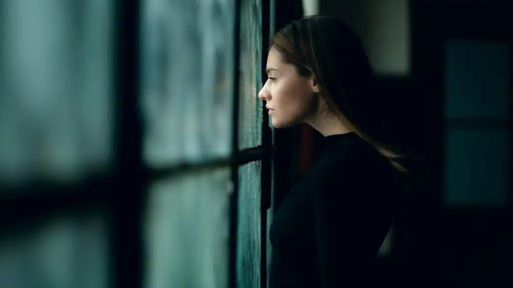 A woman in profile gazing out a window in a dimly lit room.