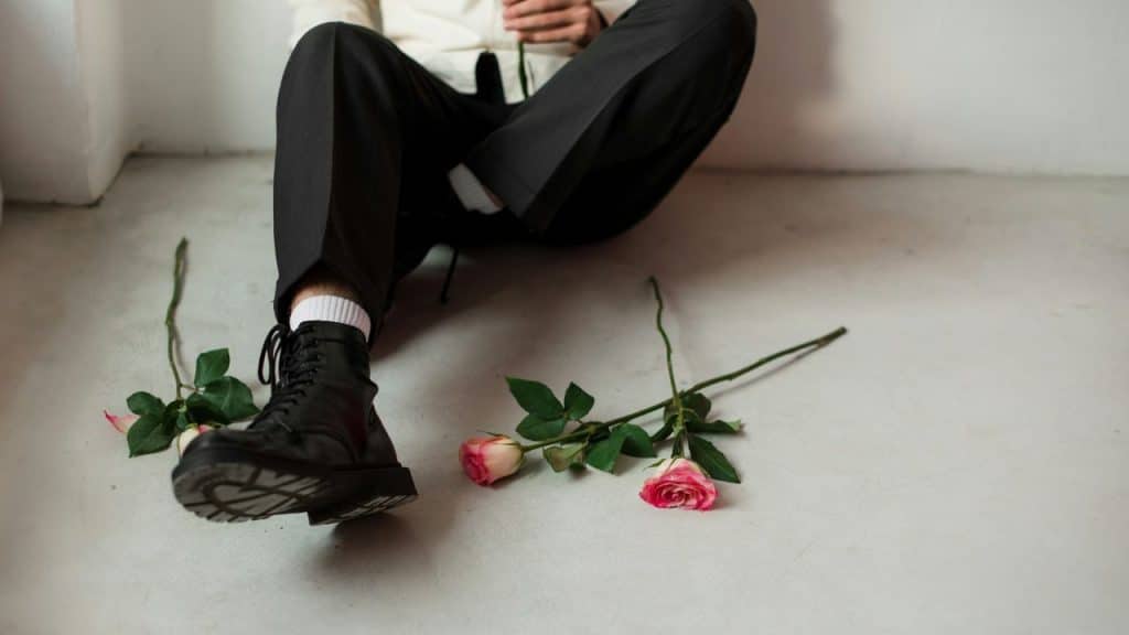 A person sits on the floor with several pink roses scattered on the ground around them.