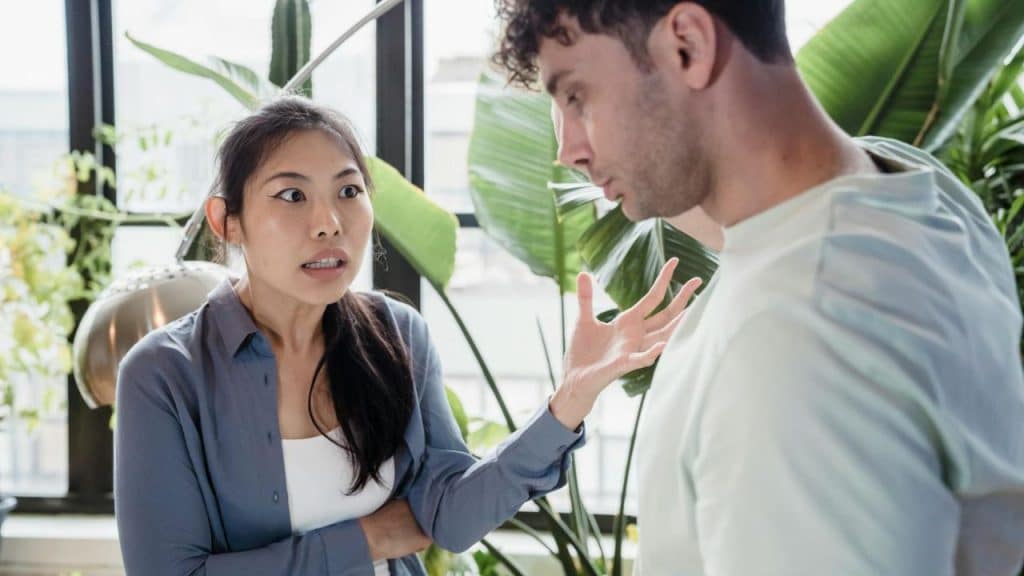 A woman with a surprised expression talks to a man while gesturing with her hand.