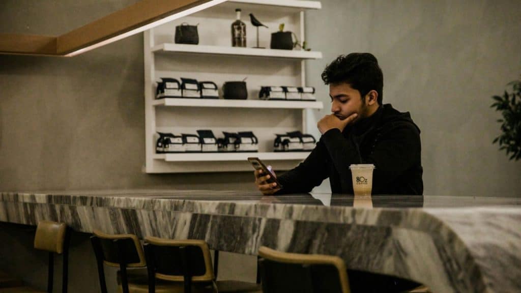 A man sits at a marble counter in a cafe looking down at a smartphone.