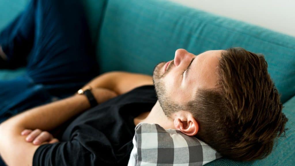 A man lying on a couch with his eyes closed, appearing relaxed or asleep.