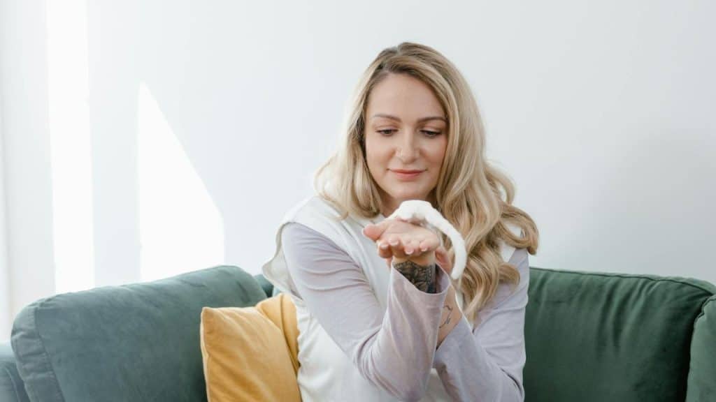 A blonde woman sitting on a green couch holds a small white rat in her hand.