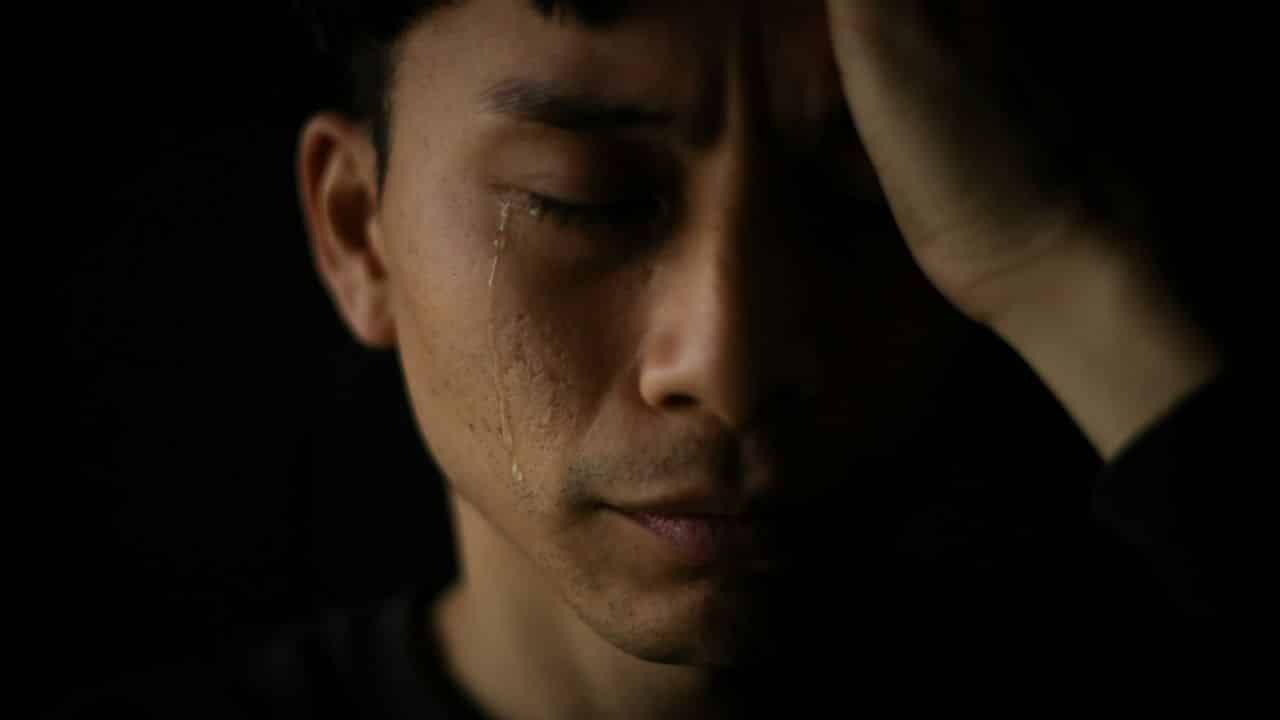 A close-up of a man with his eyes closed, a single tear running down his cheek.