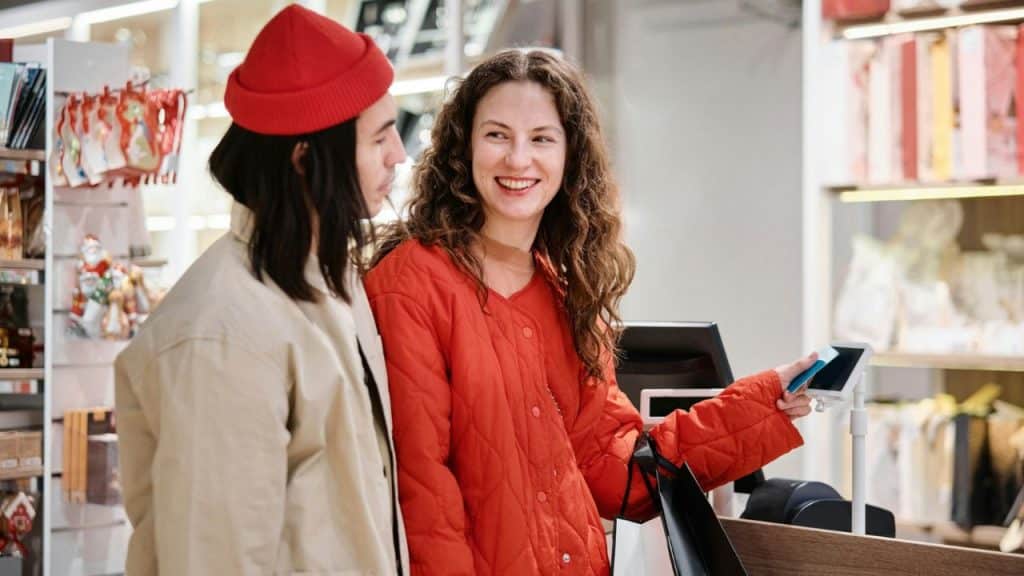 A woman in a red jacket smiles while using a card at a payment terminal.