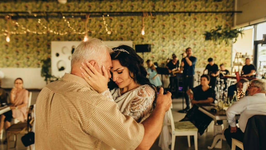 A man and a woman hugging and crying with each other in a room full of people.