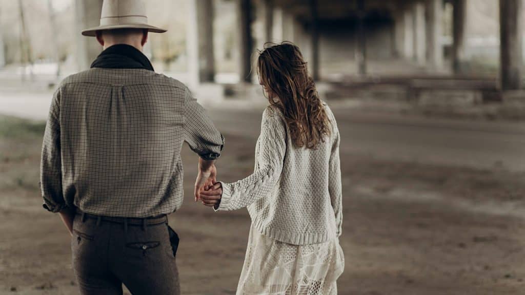 A handsome Texas cowboy man in a white hat holding hands with a beautiful woman in a white dress.