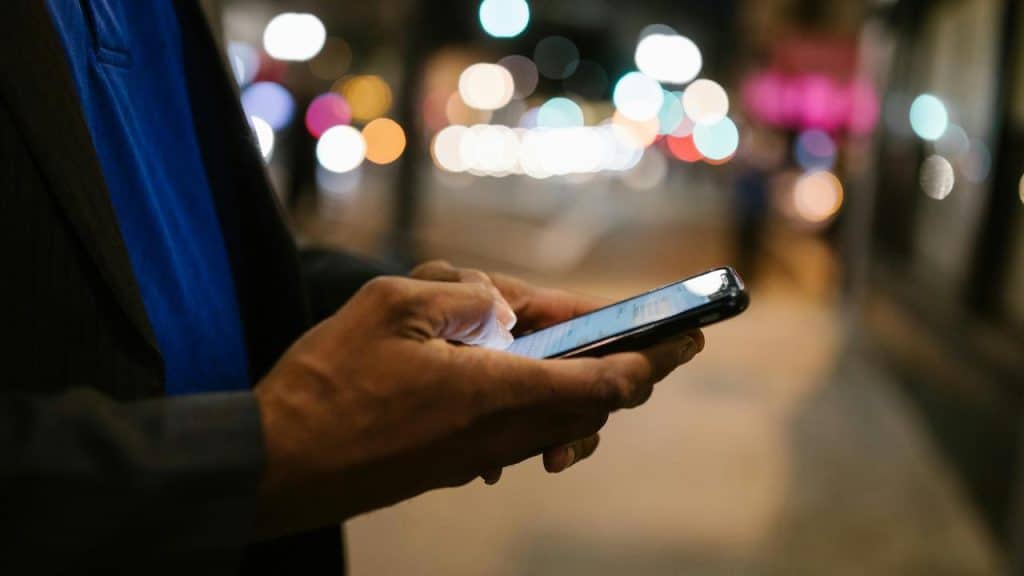 A person uses a smartphone on a city street at night.
