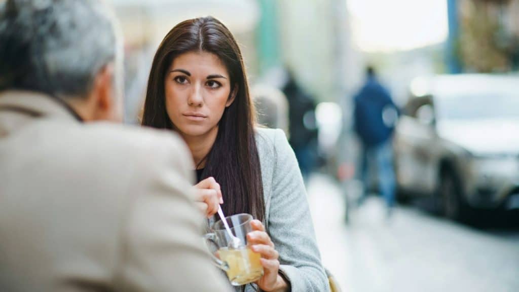 A woman with long dark hair stirs a drink while looking at a man.