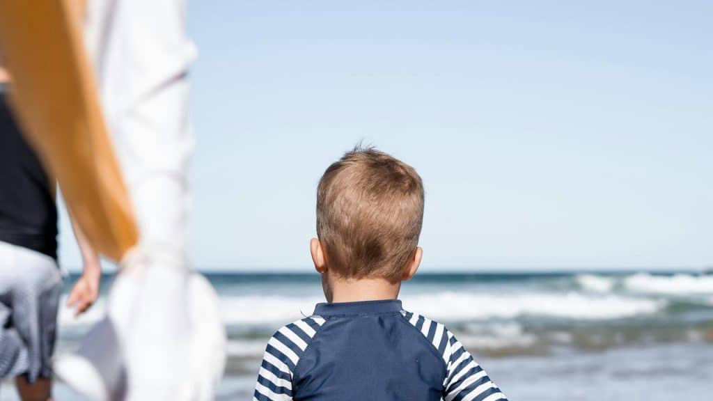 A child in a striped shirt standing on a beach.
