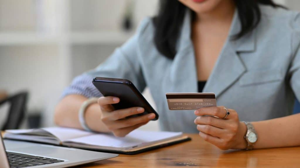 A person holding a credit card and smartphone for online payment.