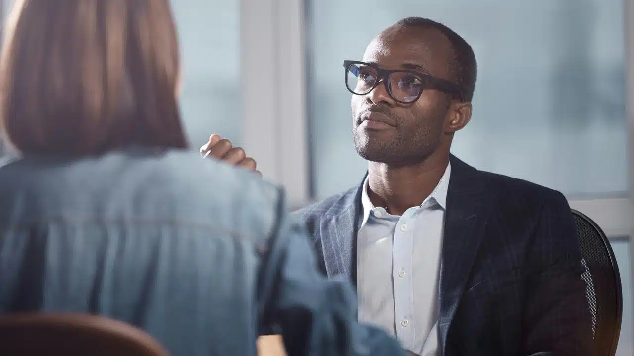 A man in glasses and a suit listening to a woman during a conversation.